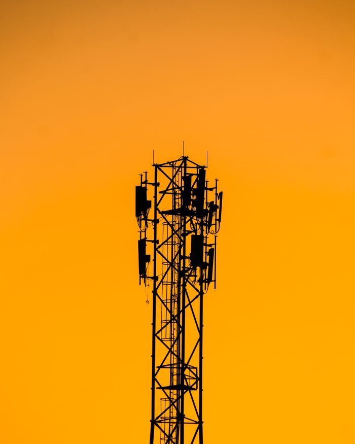 Services A telecommunication tower silhouetted against a vibrant orange sunset sky in India.