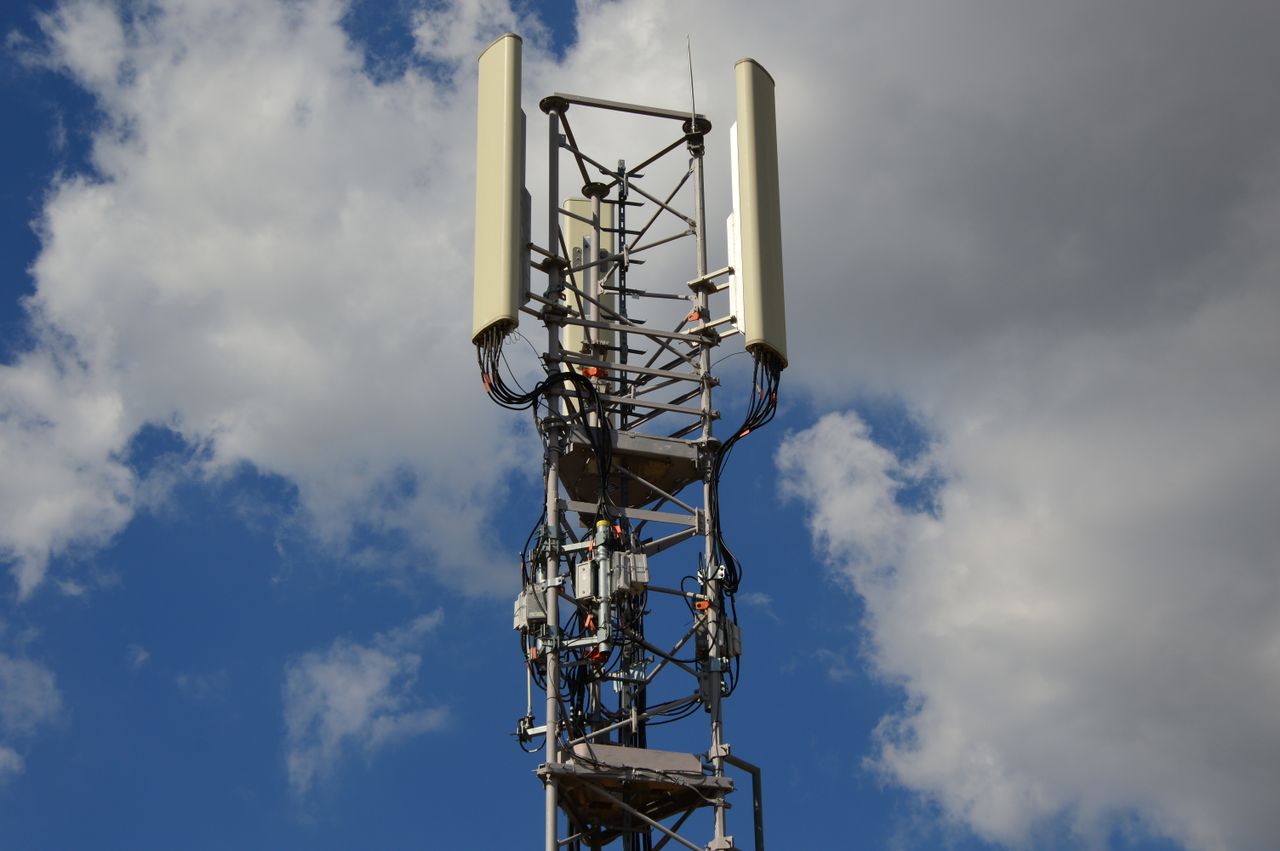Home High-angle view of a modern cell tower with technology components against a blue sky with clouds.