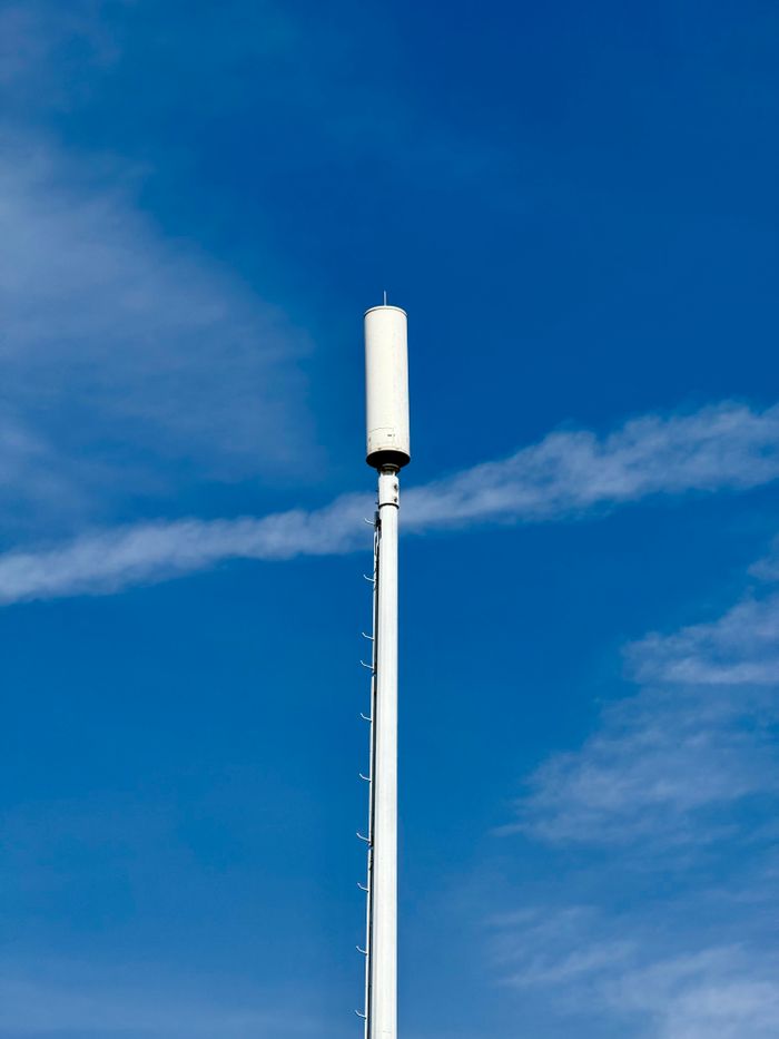 About A tall cell tower set against a clear blue sky, symbolizing communication and technology.