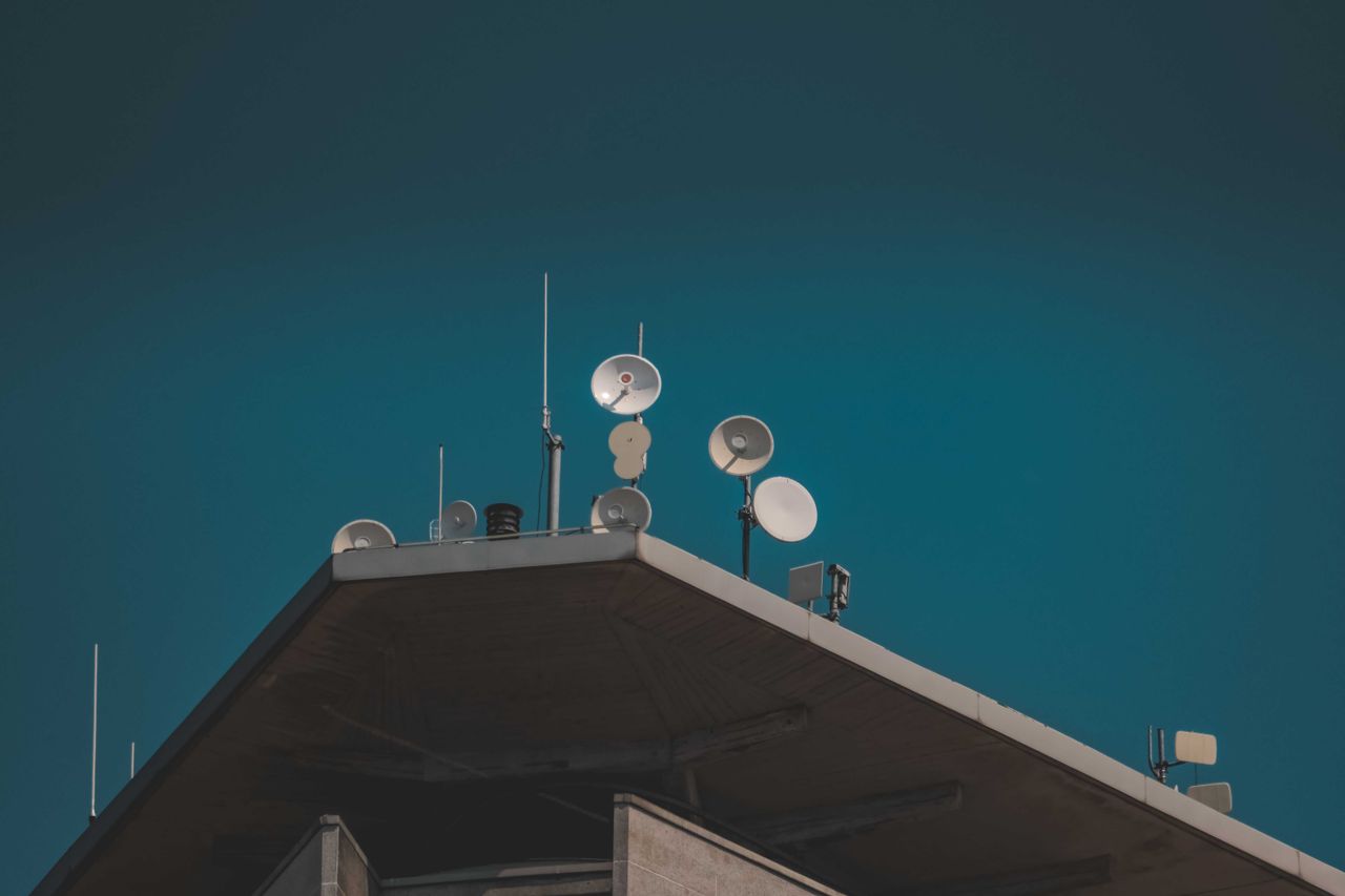 About A low-angle view of communication dishes and antennas on a building against a clear blue sky.